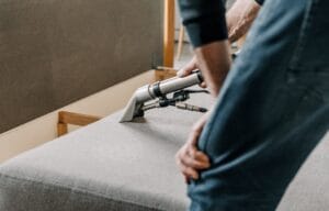 Zbliżenie na ręce fachowca z firmy Turboszczotka przesuwającego ssawkę ekstrakcyjną po szarym materiale – w trakcie profesjonalnego czyszczenia kanapy i materaca w Gdyni.